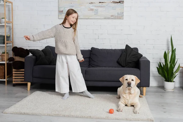 Full length of joyful child playing with labrador dog on carpet in living room — Stock Photo