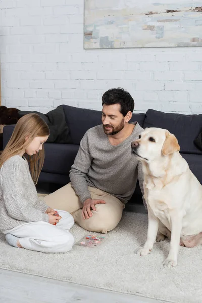 Preteen girl with smiling bearded man sitting on floor carpet near eye shadows palette and labrador dog — Foto stock