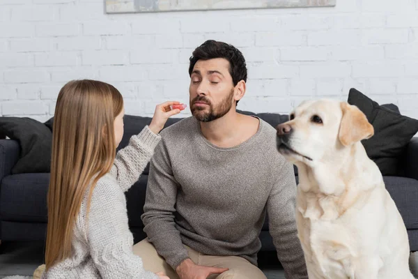 Preteen girl holding lip gloss while playing with bearded father near labrador dog — Stock Photo
