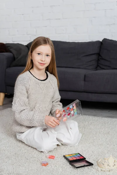 Happy preteen girl sitting on carpet and holding makeup palette — Stock Photo