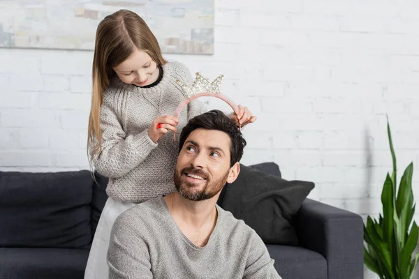 Happy kid wearing crown on head of cheerful father with beard — стоковое фото