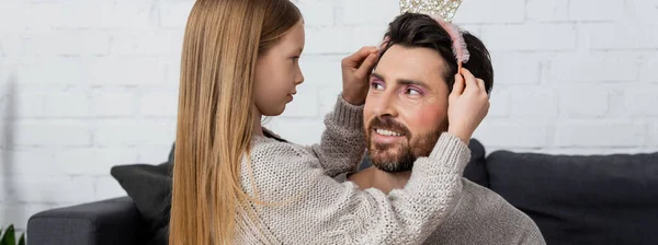 Happy girl wearing toy crown on head of father in living room, banner — Stock Photo