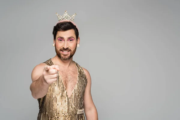 Hombre alegre con corona de juguete en la cabeza y traje de vestido de princesa señalando con el dedo aislado en gris — Stock Photo