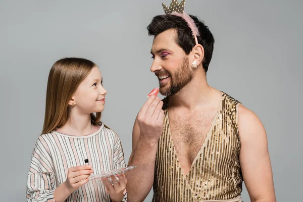Cheerful father in crown applying lip gloss and looking at happy daughter while playing beauty game isolated on grey — Stock Photo