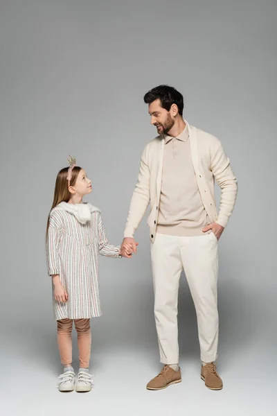 Full length of happy man holding hands of kid in crown and standing with hand in pocket on grey — Stock Photo