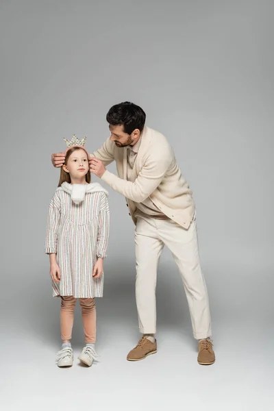 Full length of bearded father adjusting crown of daughter in dress on grey — Stock Photo
