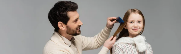 Happy bearded father brushing hair of smiling daughter isolated on grey, banner — Stock Photo