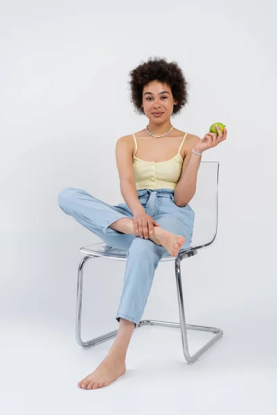 Афроамериканська жінка, яка тримає свіже яблуко, сидячи на сірому фоні. — стокове фото