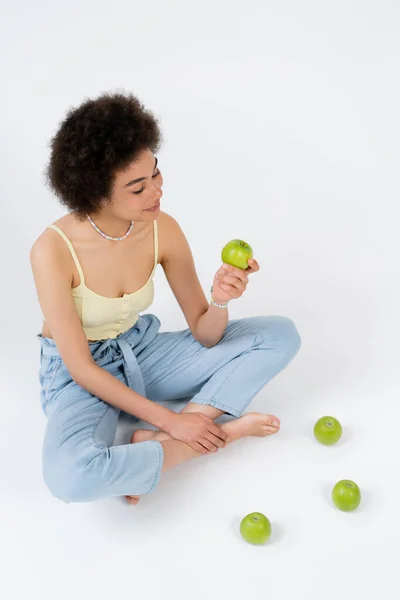 Vue en angle élevé de la femme afro-américaine tenant la pomme tout en étant assis sur fond gris — Photo de stock