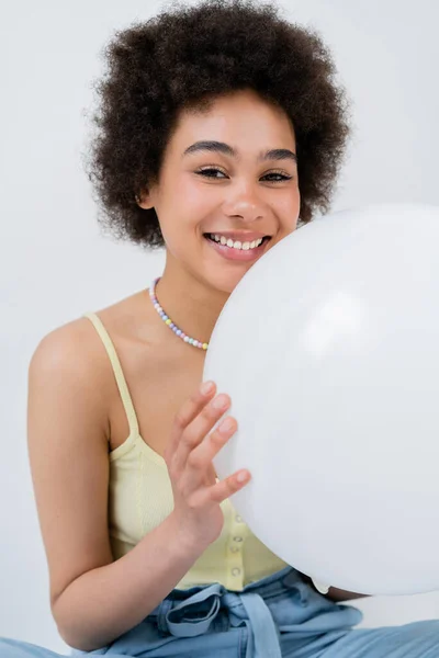 Retrato de mujer afroamericana positiva sosteniendo globo aislado en gris - foto de stock