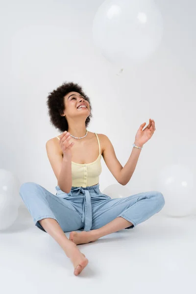 Positive african american woman throwing balloon on grey background — Stock Photo