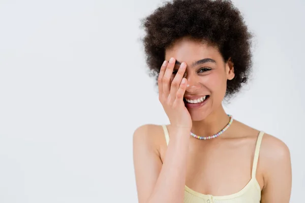 Femme afro-américaine positive touchant le visage isolé sur le gris — Photo de stock