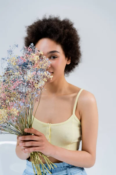 Afroamerikanerin mit Blumen in der Nähe des Gesichts auf grauem Hintergrund — Stockfoto