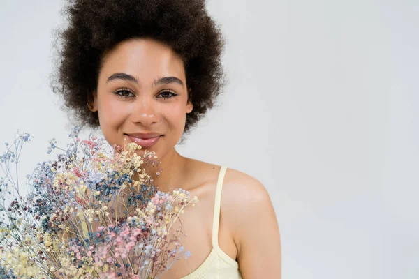 Smiling african american woman looking at camera near baby breath flowers isolated on grey — Stock Photo