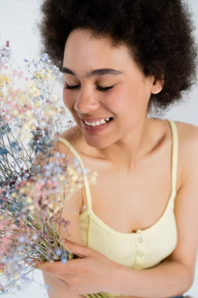Mujer afroamericana feliz sosteniendo flores de aliento de bebé aisladas en gris - foto de stock