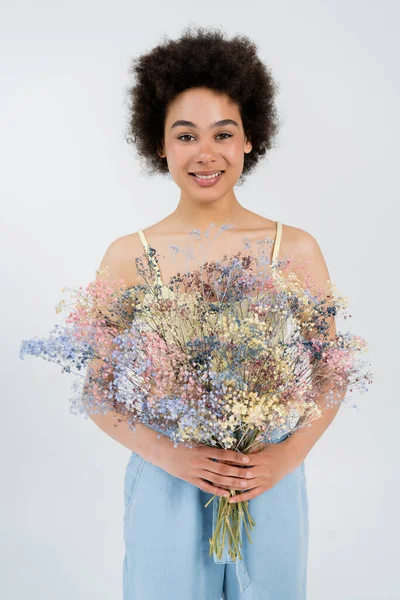 Fröhliche afrikanisch-amerikanische Frau mit Blumen in grau — Stockfoto