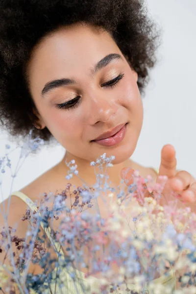 Retrato de una joven afroamericana con maquillaje natural tocando flores de aliento de bebé aisladas en gris - foto de stock
