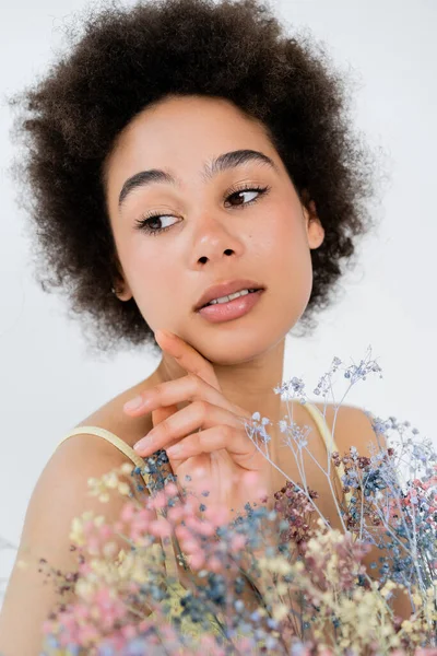 Портрет африканської жінки з Америки, яка торкається обличчя біля квіток з диханням, ізольованих на сірих — стокове фото