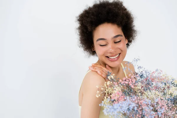 Mujer afroamericana feliz tocando hombro cerca de flores aliento bebé aislado en gris, bandera - foto de stock