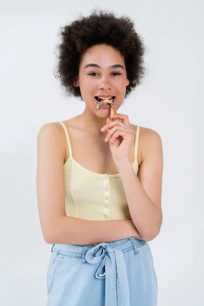 Modelo afroamericano sosteniendo colorido bastón de caramelo aislado en gris - foto de stock