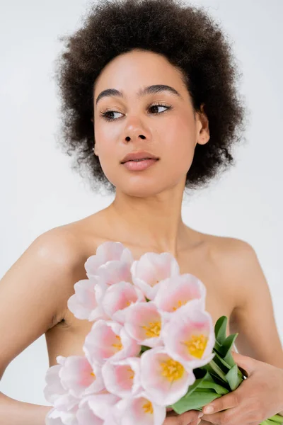 Retrato de mujer afroamericana con hombros desnudos sosteniendo tulipanes aislados en gris - foto de stock