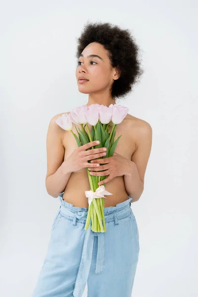 Mujer afroamericana con pecho desnudo sosteniendo flores de tulipán aisladas en gris - foto de stock