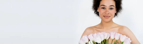 Petty african american woman with naked shoulders posing with tulips isolated on grey, banner — Stock Photo