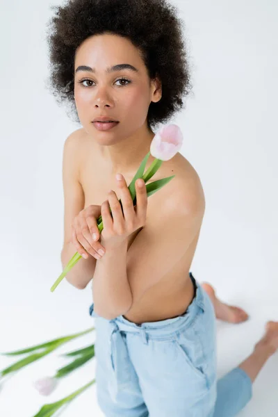 Femme afro-américaine aux épaules nues tenant une tulipe rose sur fond gris — Photo de stock