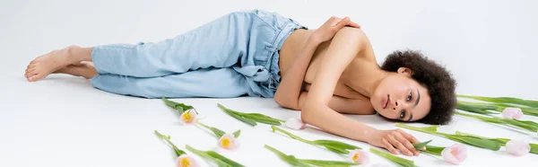 Modèle africain américain torse nu couché près des tulipes roses sur fond gris, bannière — Photo de stock