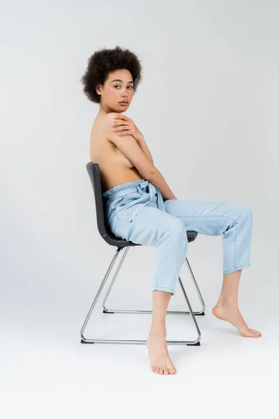 Hemdlose Afroamerikanerin posiert auf Stuhl vor grauem Hintergrund — Stockfoto