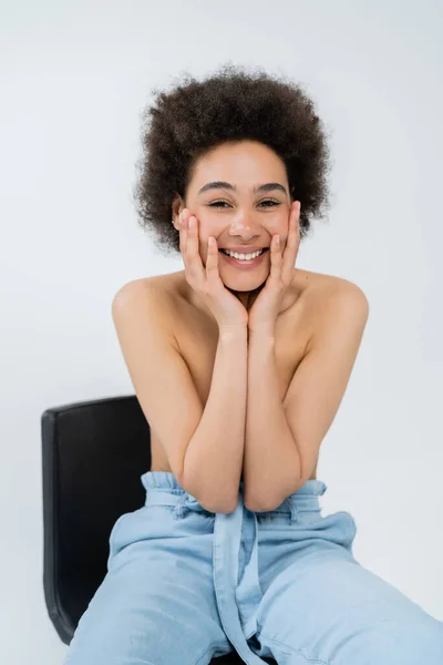 Lächelnde und hemdlose Afroamerikanerin berührt Gesicht isoliert auf grau — Stockfoto