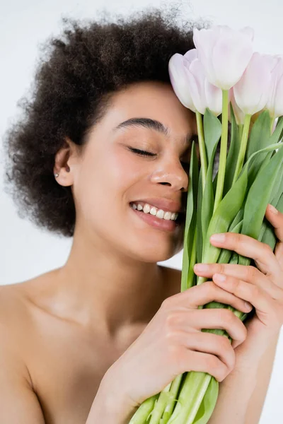 Lächelnde afrikanisch-amerikanische Frau mit nackten Schultern, die einen Strauß Tulpen auf grau isoliert hält — Stockfoto