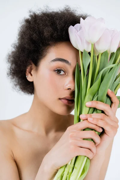Shirtless african american woman holding bouquet of tulips near face isolated on grey — Stock Photo