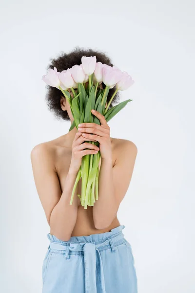 Femme afro-américaine torse nu tenant des tulipes près du visage isolé sur gris — Photo de stock