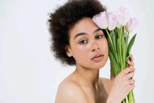 Retrato de modelo afroamericano con hombros desnudos sosteniendo tulipanes aislados en gris - foto de stock