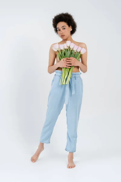 Американка без рубашки и босиком держит тюльпаны, стоя на сером фоне — стоковое фото