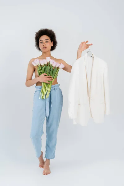 Shirtless african american woman holding tulips and jacket on grey background — Stock Photo
