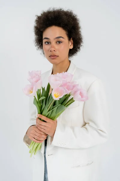 Modello afroamericano in giacca contenente bouquet di tulipani isolati su grigio — Foto stock