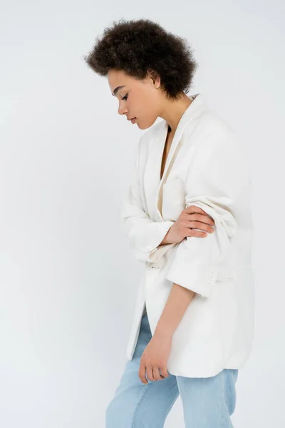 Vista lateral de la mujer afroamericana de moda enrollándose en la manga de la chaqueta aislada en gris - foto de stock