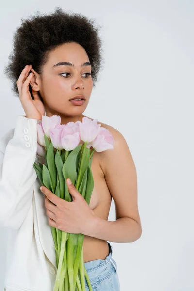 Stylish african american woman in jacket with naked shoulder holding flowers isolated on grey — Stock Photo