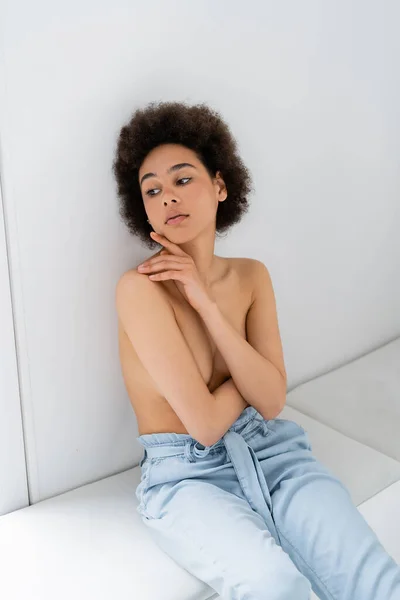 Joven modelo afroamericano sin camisa sentada sobre alféizar de ventana sobre fondo gris - foto de stock