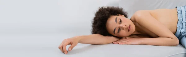 Modèle afro-américain torse nu couché sur un canapé sur fond gris, bannière — Photo de stock