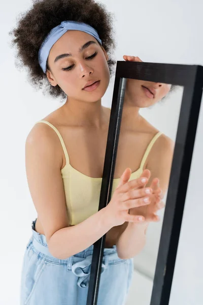 Африканская американка в повязке на голове, касающееся зеркала, изолированного на сером — стоковое фото