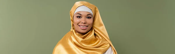 Retrato de mulher multirracial sorridente em hijab amarelo olhando para a câmera isolada em verde, banner — Fotografia de Stock