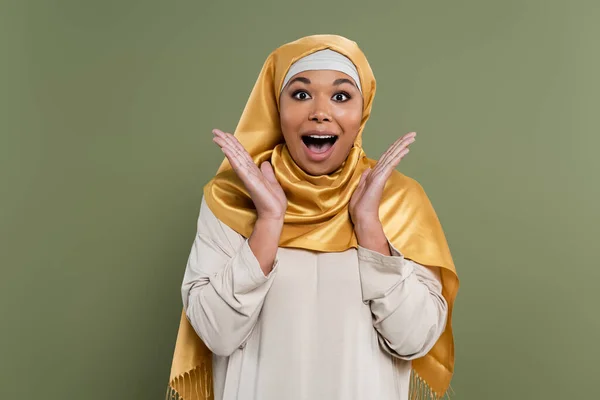 Astonished multiracial woman in hijab looking at camera isolated on green — Stock Photo