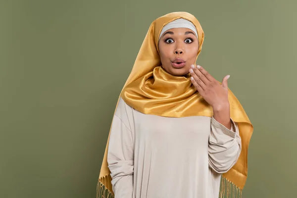 Impresionada mujer multirracial en hijab mirando a la cámara aislada en verde - foto de stock