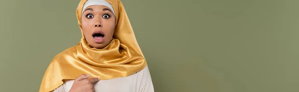 Donna multirazziale scioccata in hijab giallo che punta con il dito verso se stessa isolata sul verde, striscione — Foto stock