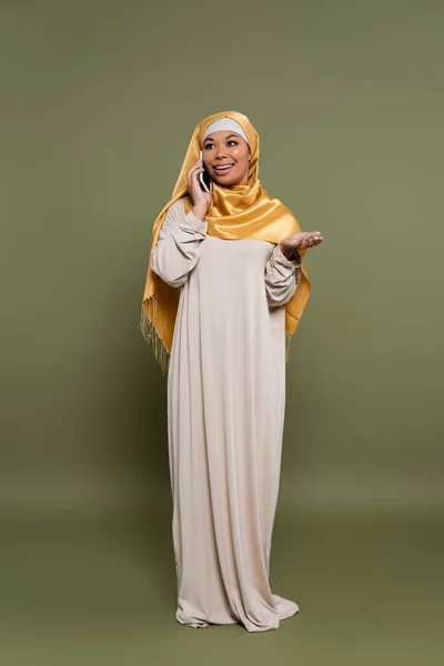 Полная длина многорасовой женщины в хиджабе говорить по мобильному телефону на зеленом фоне — стоковое фото