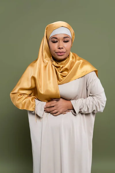 Mujer multiracial en hiyab sintiendo dolor de estómago sobre fondo verde - foto de stock