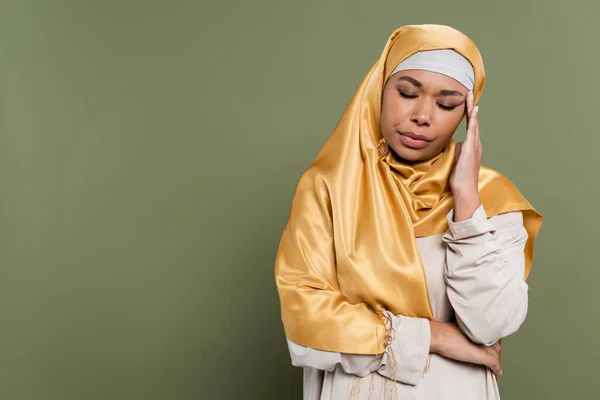 Joven mujer multirracial en hiyab que sufre de dolor de cabeza sobre fondo verde - foto de stock